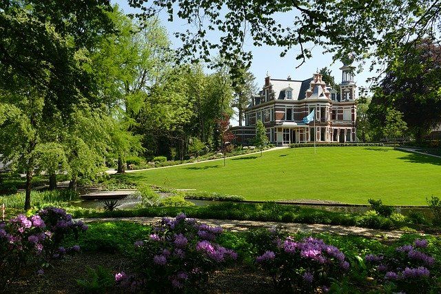 Ein Herrenhaus mit einem kurzen Rasen und Rhododendron Pflanzen.